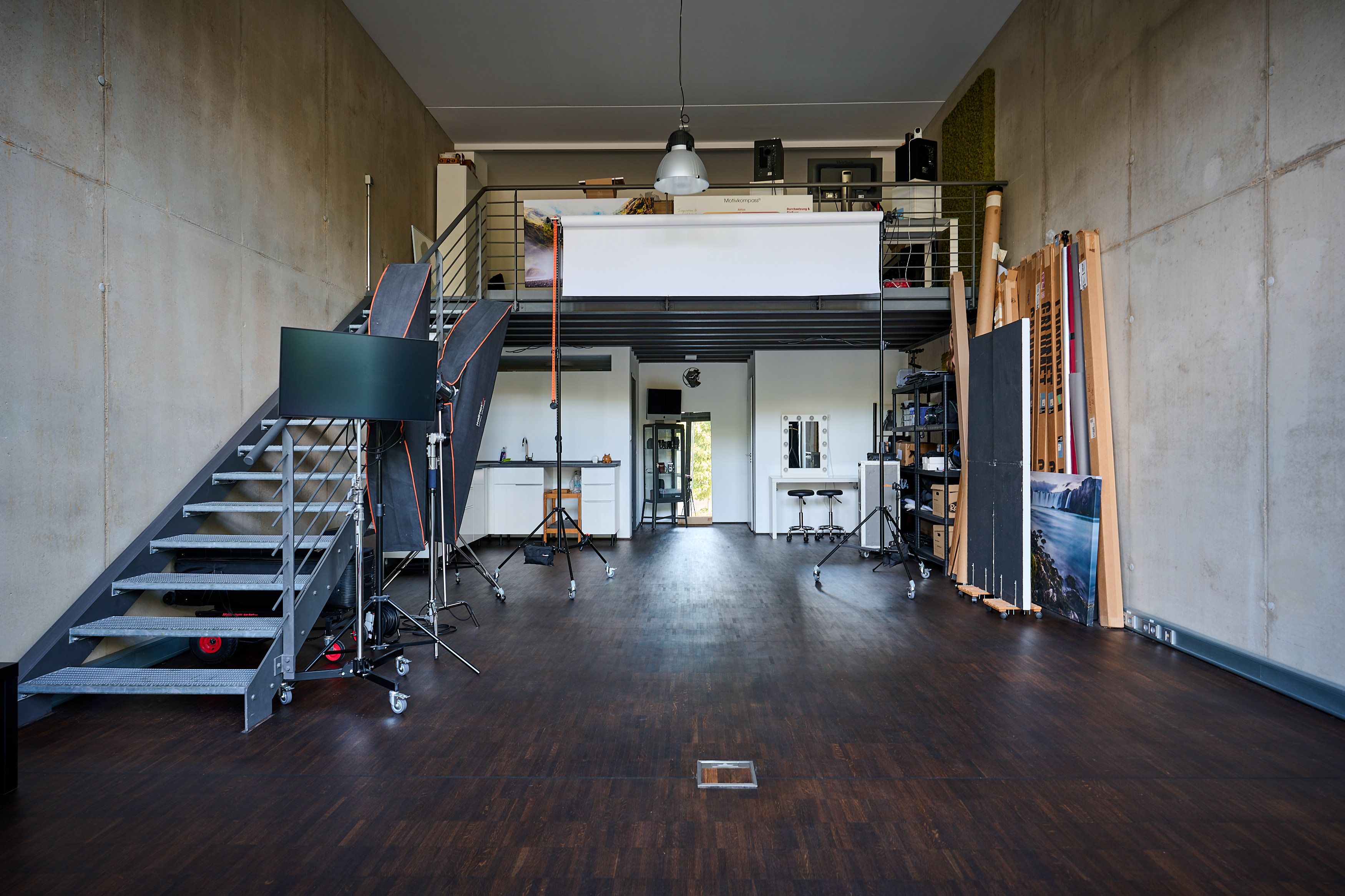 Blick in das Mietstudio Lichtreich in Köln-Zollstock: freie Setfläche, Empore und Treppe, Betonwände, dunkler Holzboden.